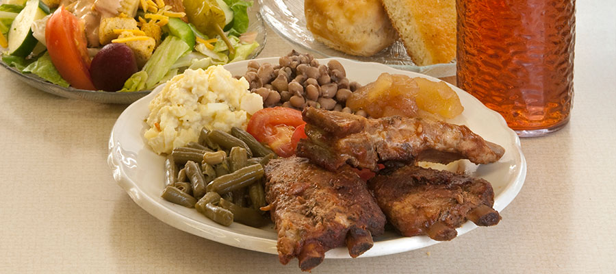 plate of ribs, vegetables with salad and cornbread and tea